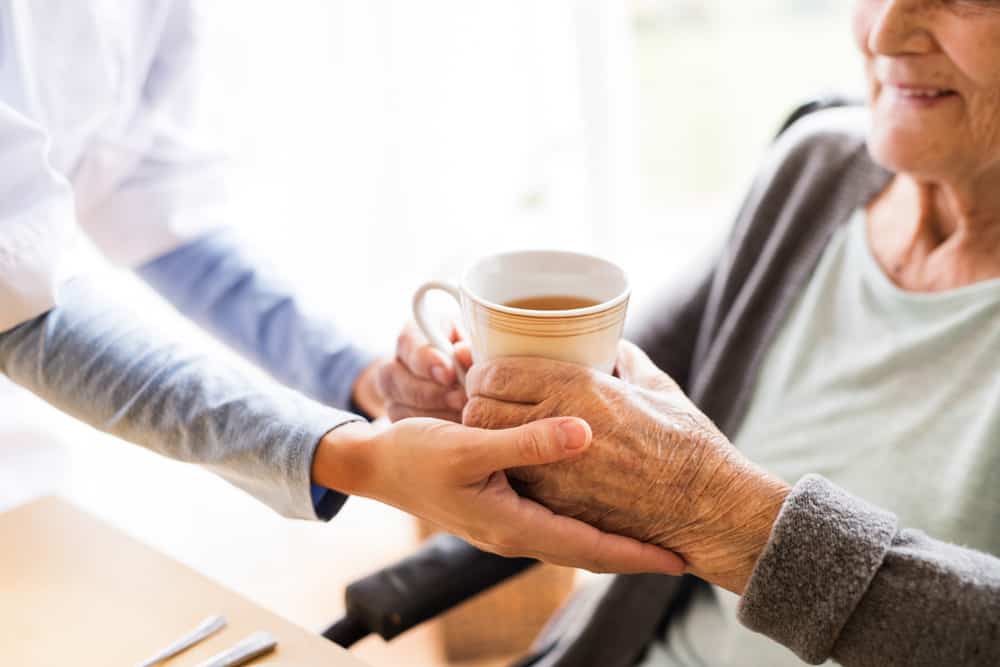Aged care worker offering coffee to her elderly client