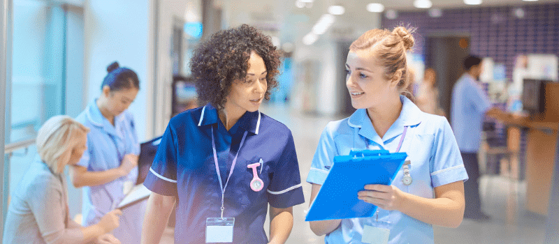 Two female healthcare works look over clipboard